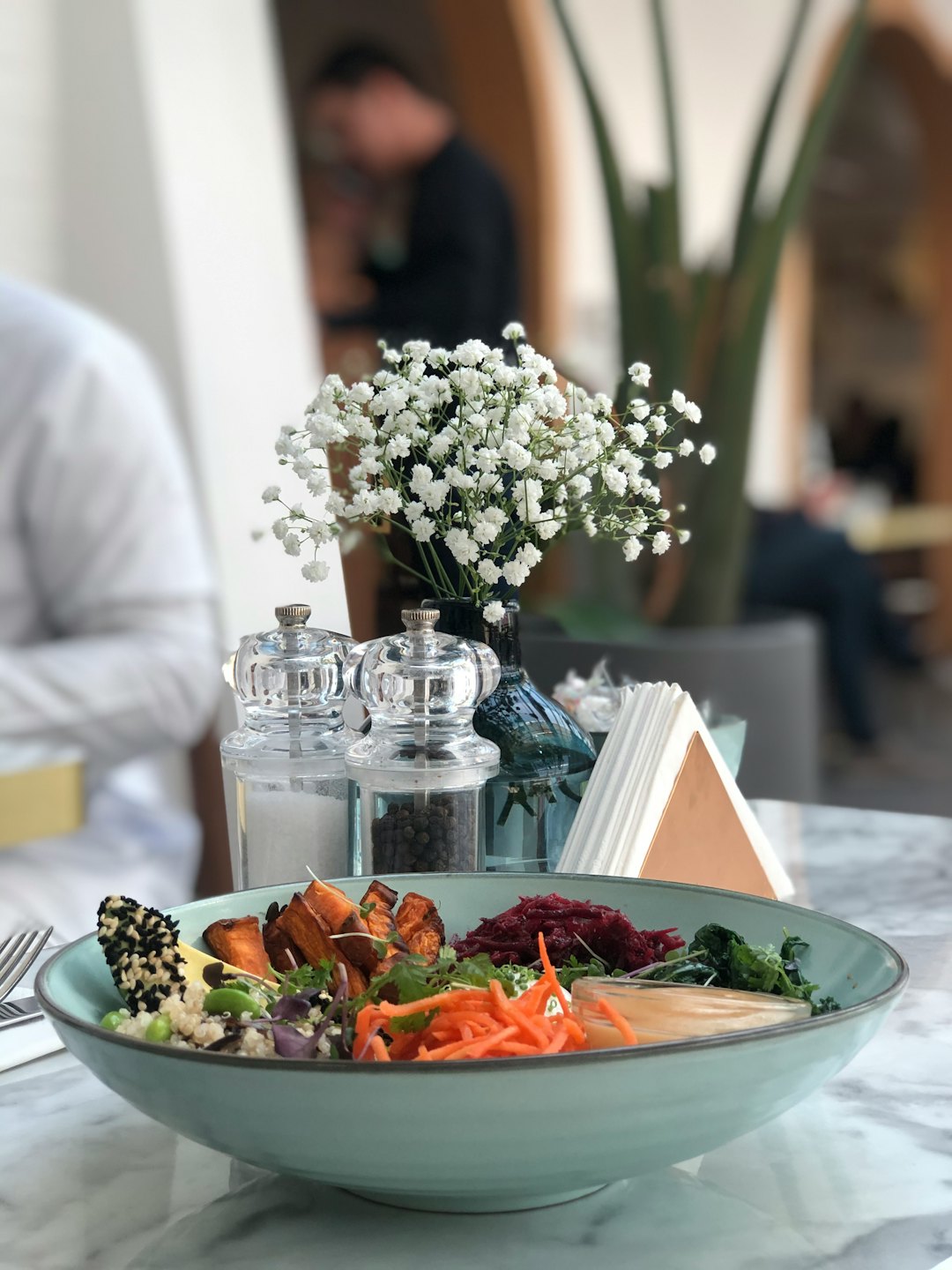 Healthy meal bowl with sweet potatoes, cabbage, carrots, quinoa, and kale on a marble table.